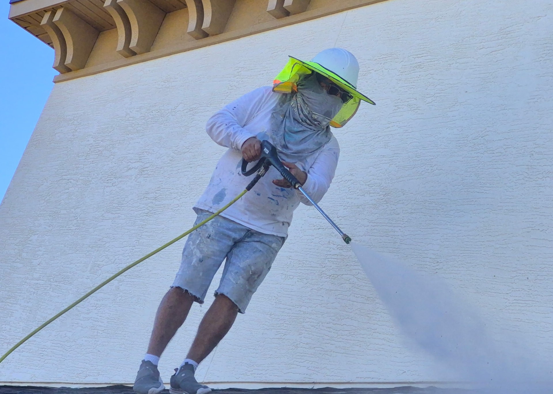 Crew member power washing a stucco wall from a rooftop