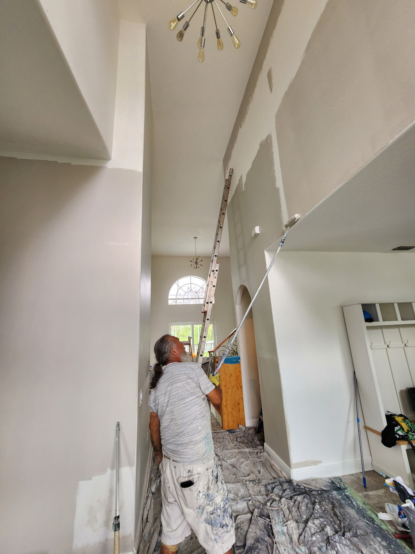 Jesús Gil painting the tall interior walls of a two-story home